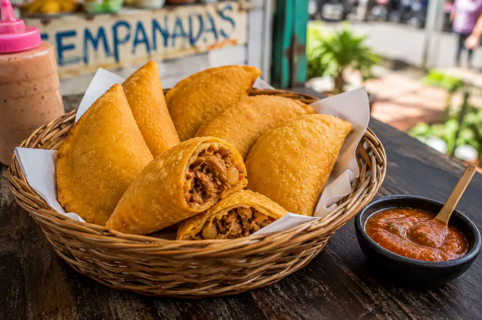 Colombian empanadas in a woven basket with ají sauce