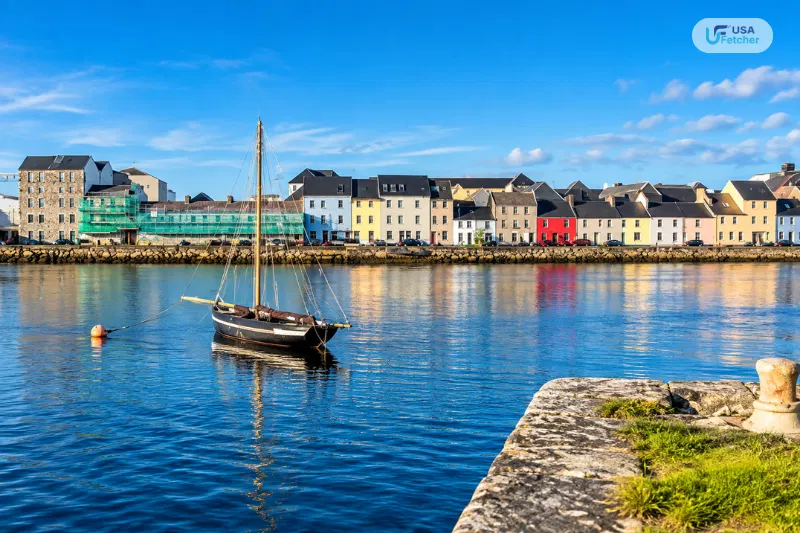 Colorful Galway waterfront with a sailboat on Galway Bay under a clear blue sky