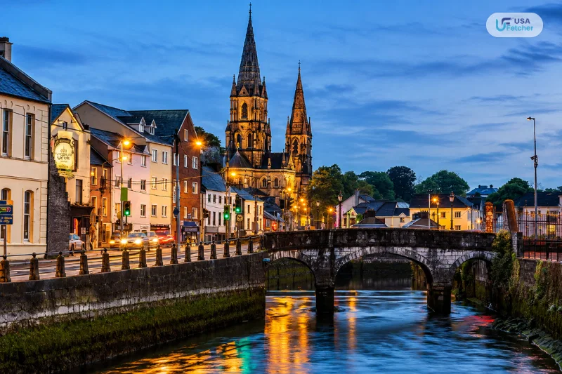 Evening view of Cork city with a historic stone bridge, river, and illuminated cathedral in Ireland