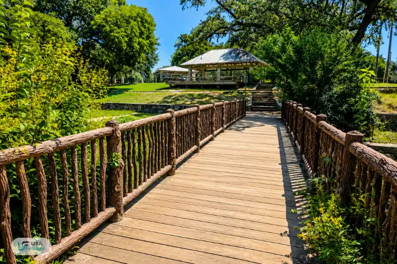 Scenic wooden bridge leading to a picnic pavilion in New Braunfels TX Landa Park surrounded by lush greenery