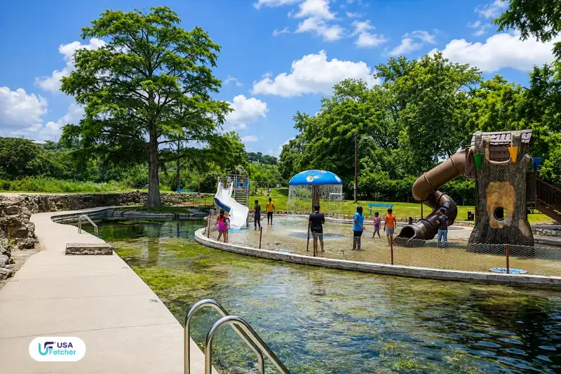 Family-friendly splash pad and spring-fed swimming area at New Braunfels TX Landa Park with playground, slides, and shaded trees